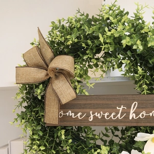 Artificial eucalyptus wreath with a home sweet home sign and a burlap bow on a white background