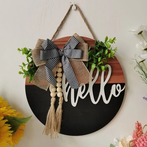 Detail of 3D wooden door sign with hello script, rustic bow, and green leaves decoration