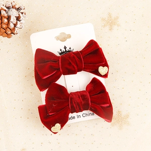 Red velvet Christmas bow hair clips with golden heart accents on a white display card