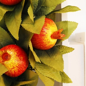Artificial autumn pomegranate wreath with vibrant red fruits and green leaves for home decor