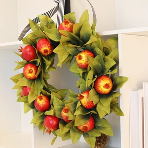 Detail of faux pomegranate wreath with green leaves and a black-white striped ribbon loop