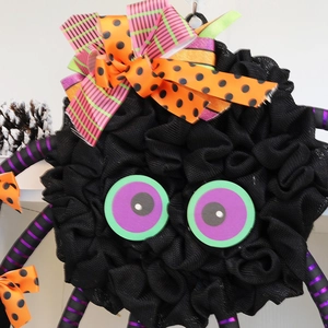 Halloween spider wreath pendant with green eyes, striped legs and decorative festive bows