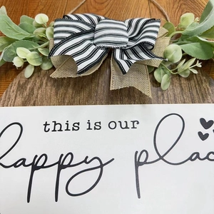 Detail of wooden home sign with bow, greenery and this is our happy place text