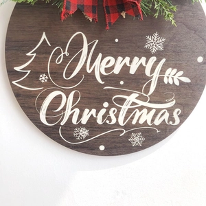 Wooden Merry Christmas welcome sign with buffalo plaid bow and artificial pine greenery