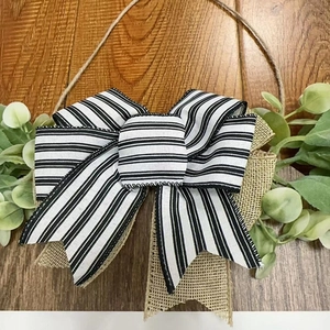 Detail of striped ribbon bow with green eucalyptus leaves on a rustic wooden welcome sign