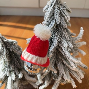 Macro detail of disco ball ornament with red knitted Santa hat on a frosted tree