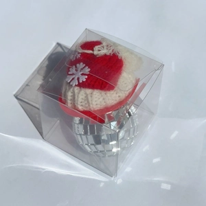 Close-up of a disco ball Christmas ornament with red knit hat in a clear gift box