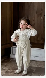 Détail de chemise bébé fleurie avec col en dentelle et salopette beige avec motif cœur