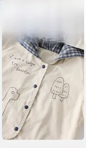 Detail of beige cotton baby jacket with embroidered text and blue checkered lining