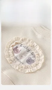 Détail d'un sweat pour bébé avec bordures en dentelle et broderie d'ours en peluche