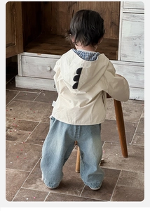 Detail view of baby beige hooded jacket featuring 3D dinosaur spikes on the back