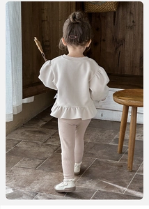 Detail of girl's cream puff-sleeve sweatshirt with ruffle hem and pink ribbed leggings