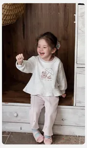 Detail of baby girl beige sweatshirt with bear print and pink joggers in a cozy setting