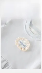 Detail of baby girl light blue cotton knit top with lace embroidery and ribbed neckline