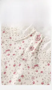 Close-up of floral baby top featuring lace collar and pink decorative buttons detail