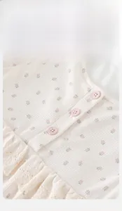 Détail du tissu gaufré à fleurs pour bébé avec boutons roses et col bordé de dentelle