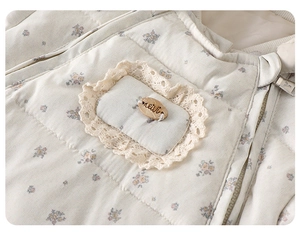 Detail of floral quilted baby winter jumpsuit showing lace trim and wood tag