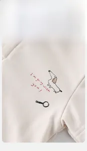 Close-up of baby polo shirt in soft beige knit cotton with embroidered dachshund and wood button