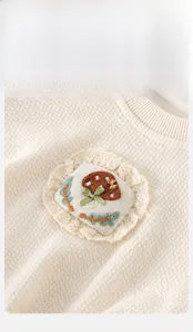 Détail du haut en maille gaufrée crème pour bébé avec broderie champignon et dentelle