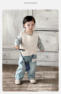 Detail of baby boy three-piece set featuring cream vest and light wash denim pants
