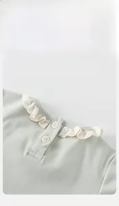 Detailed view of sage green knit baby top featuring lace trim collar and white button closure