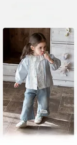 Dettaglio del colletto in pizzo floreale su camicia blu e jeans a gamba larga lavaggio chiaro
