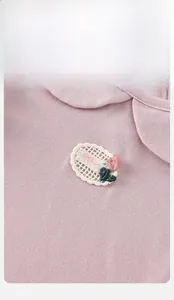 Close-up of pink baby knitted top with Peter Pan collar and rose embroidery detail