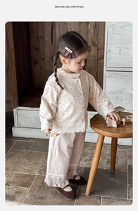 Dettaglio del bordo in pizzo sul completo pigiama beige a fiori per neonata con bottoni