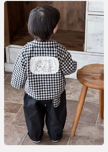 Detail of baby boy's plaid shirt with artistic text and comfortable black casual pants