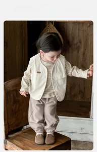 Detail of toddler corduroy vest with knit sweater and matching trousers on a wood background