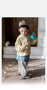 Dettaglio della felpa neonato con ricamo Happy Bee e pantaloni a righe su pavimento in legno