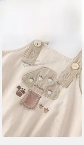 Détail de la salopette bébé beige avec broderies de champignons, écureuil et poche rose
