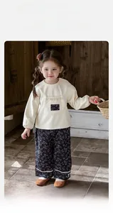 Dettaglio felpa panna per neonata con tasca floreale e pantaloni blu rifiniti in pizzo