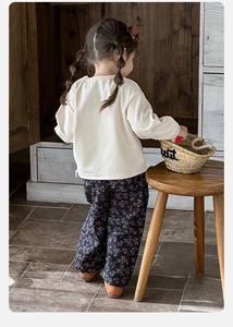Vista posteriore di bambina con felpa crema e pantaloni larghi a fiori retrò