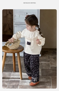 Dettaglio della felpa crema con tasca floreale e pantaloni a fiori con pizzo