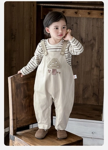 Détail d'une tenue bébé en coton avec haut rayé et salopette brodée de champignons