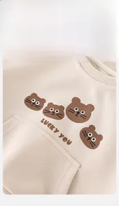 Close-up of baby beige sweatshirt with lucky bear print and kangaroo pocket detail