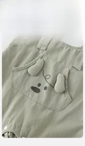 Close-up of light green baby overalls with cartoon animal pocket and button closure
