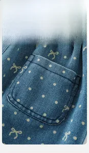 Macro detail of baby girl denim overalls featuring white polka dots and a bow pattern