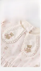 Detail of baby pink cotton dress showing Peter Pan collar with cute teddy bear and pom-poms