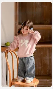 Détail du sweat à volants rose et du pantalon en jean bleu clair avec bords en dentelle