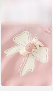 Détail d'un sweat rose pour bébé avec un grand nœud blanc et un lapin 3D brodé de marguerites
