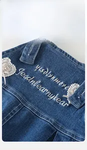 Détail de la salopette en jean bleu avec broderie blanche et perles en cœur de dentelle