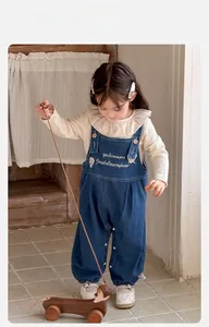 Détail de la tenue bébé fille avec haut à col volanté et salopette en jean bleu marine