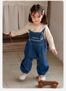 Détail d'un ensemble salopette bébé fille avec col à volants et broderie sur tissu denim bleu