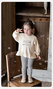 Detail of baby girl's cream ruffles sweatshirt with cartoon print and striped leggings