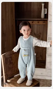 Detail of light blue baby denim overalls with striped long sleeve shirt on a wooden bench