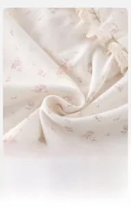 Nahaufnahme von weichem beige Babykleidungsstoff mit rosa Blumendruck und Spitzenkante