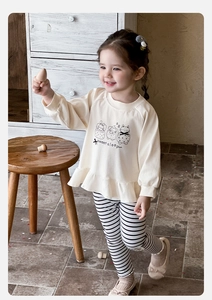 Detail view of baby girl outfit featuring beige ruffle sweatshirt with cat prints and striped leggings