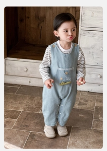 Detail of baby denim overalls with a cute crocodile embroidery and striped long sleeve shirt